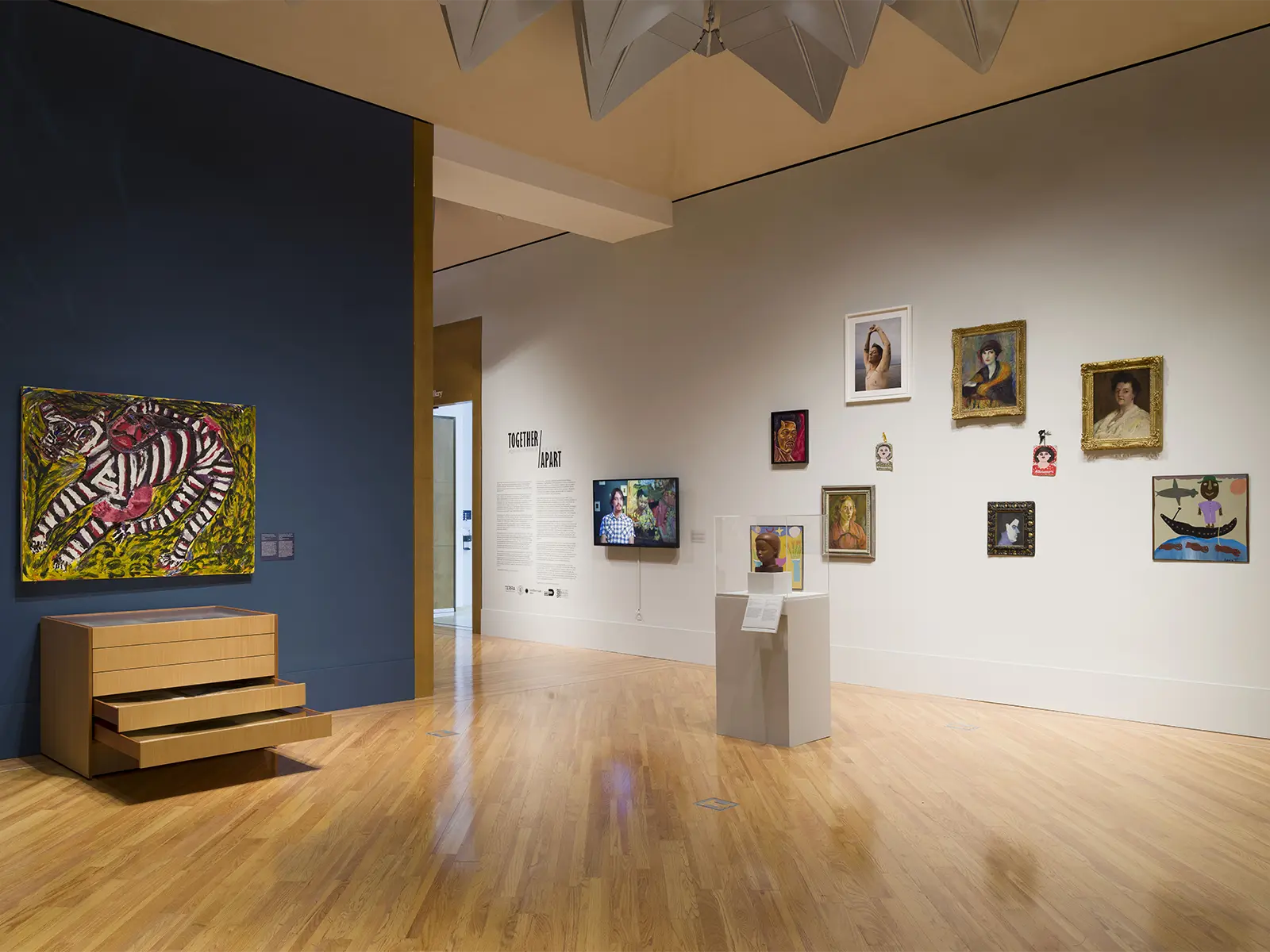 Art gallery with various paintings and a sculpture. A large, colorful zebra pattern painting is on the left, and several smaller artworks are on the right. A small sculpture is displayed on a pedestal in the center of the room.