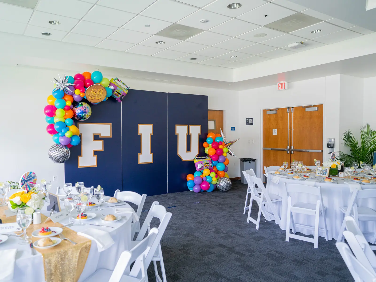 A decorated room with event tables, balloons, and an oversized sign that reads F-I-U.