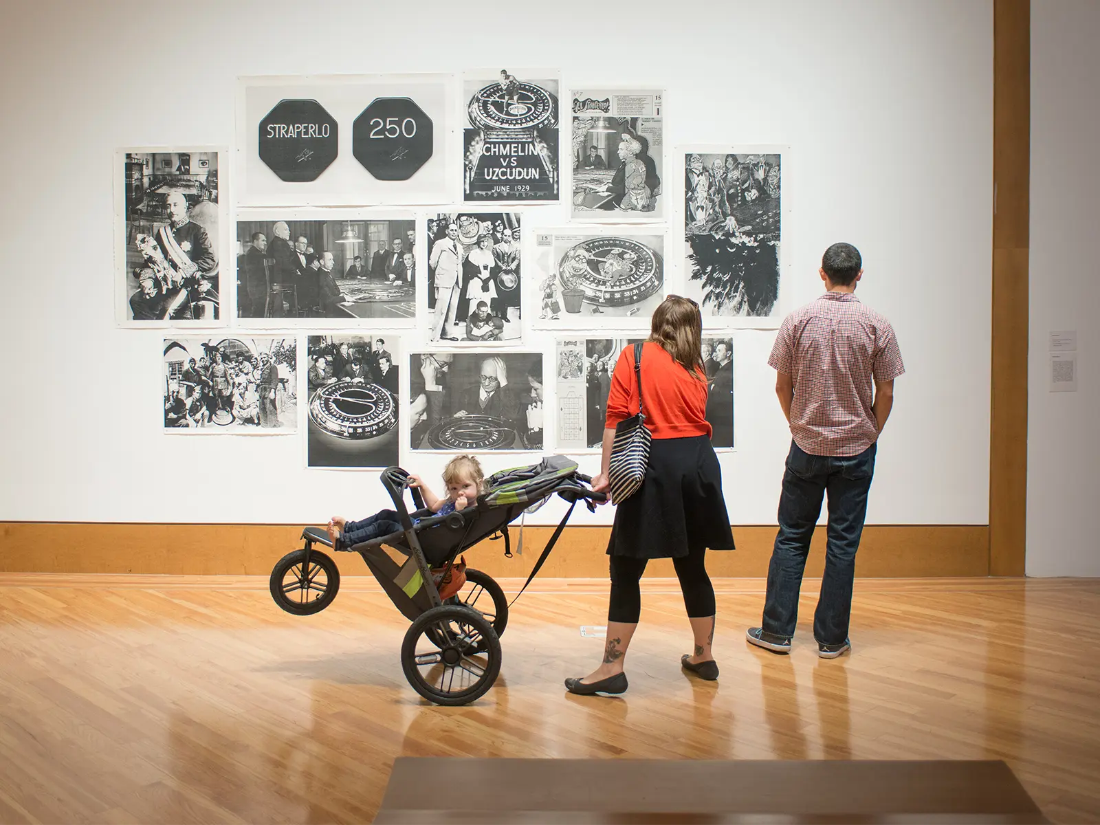 A couple with a a child in a stroller view a black-and-white photo collage at the Frost Art Museum