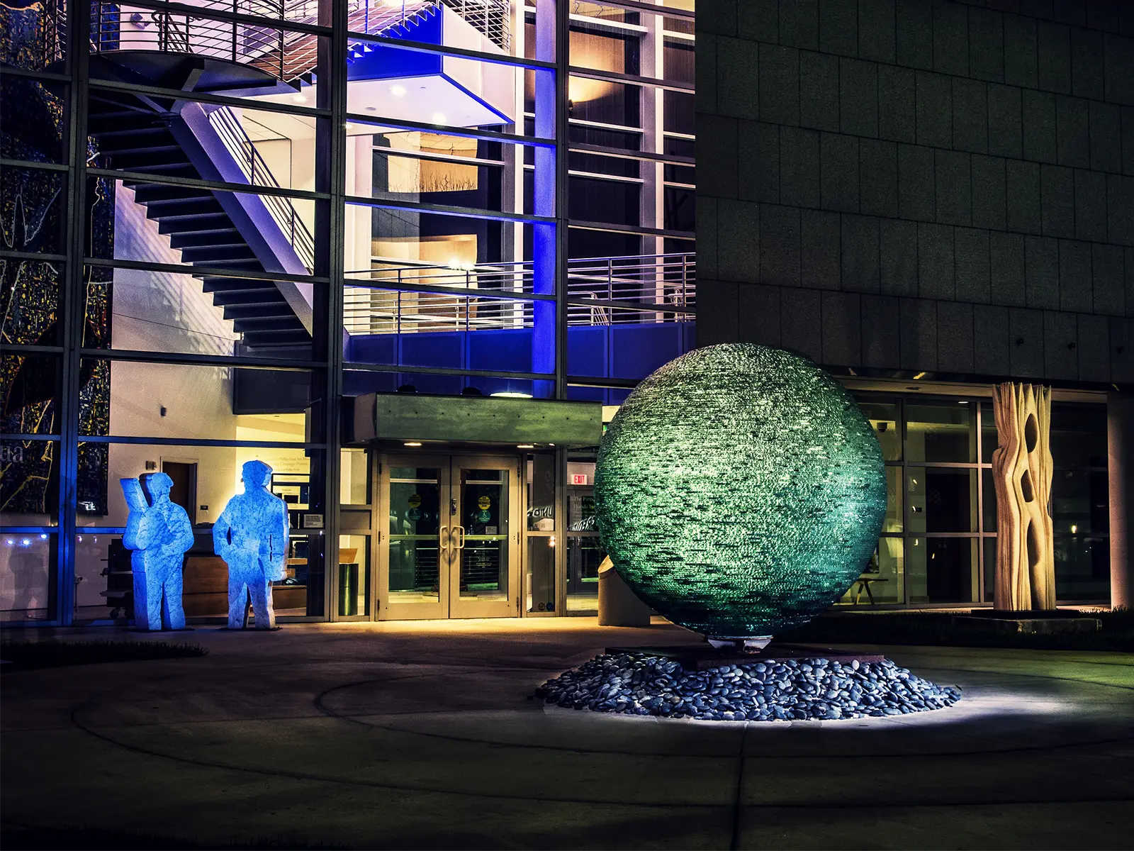 Illuminated modern building and glowing spherical sculpture at Frost Art Museum at night