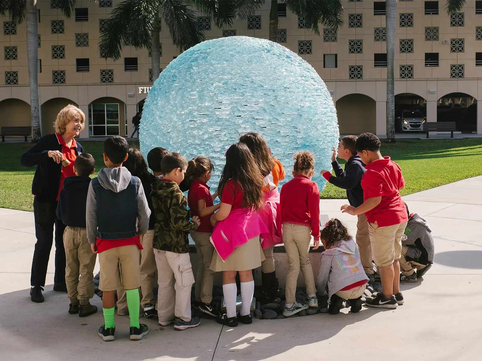 Group of students in red uniforms interacting with a large, translucent blue sphere outside the Frost Art Museun–FIU..