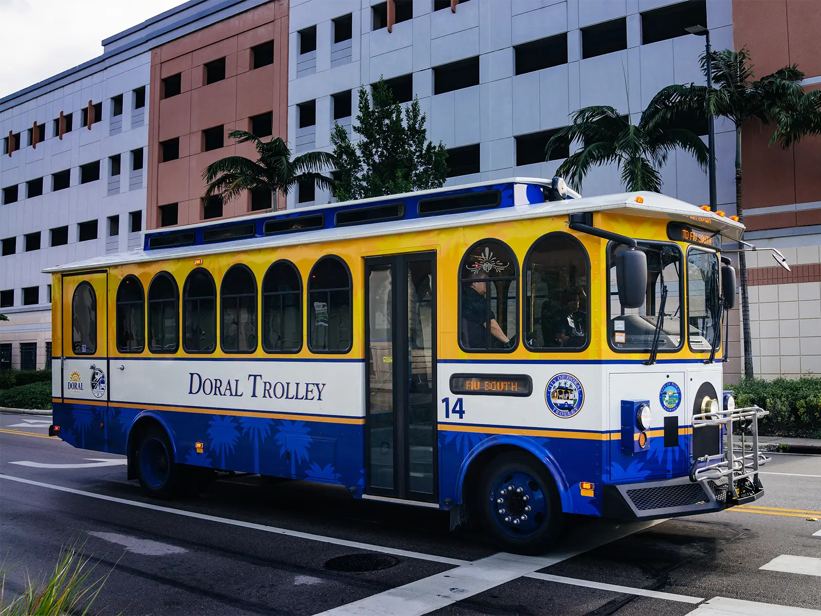 A blue and yellow Doral Trolley with the number 14 on its side with an FIU parking garage visible in the background.