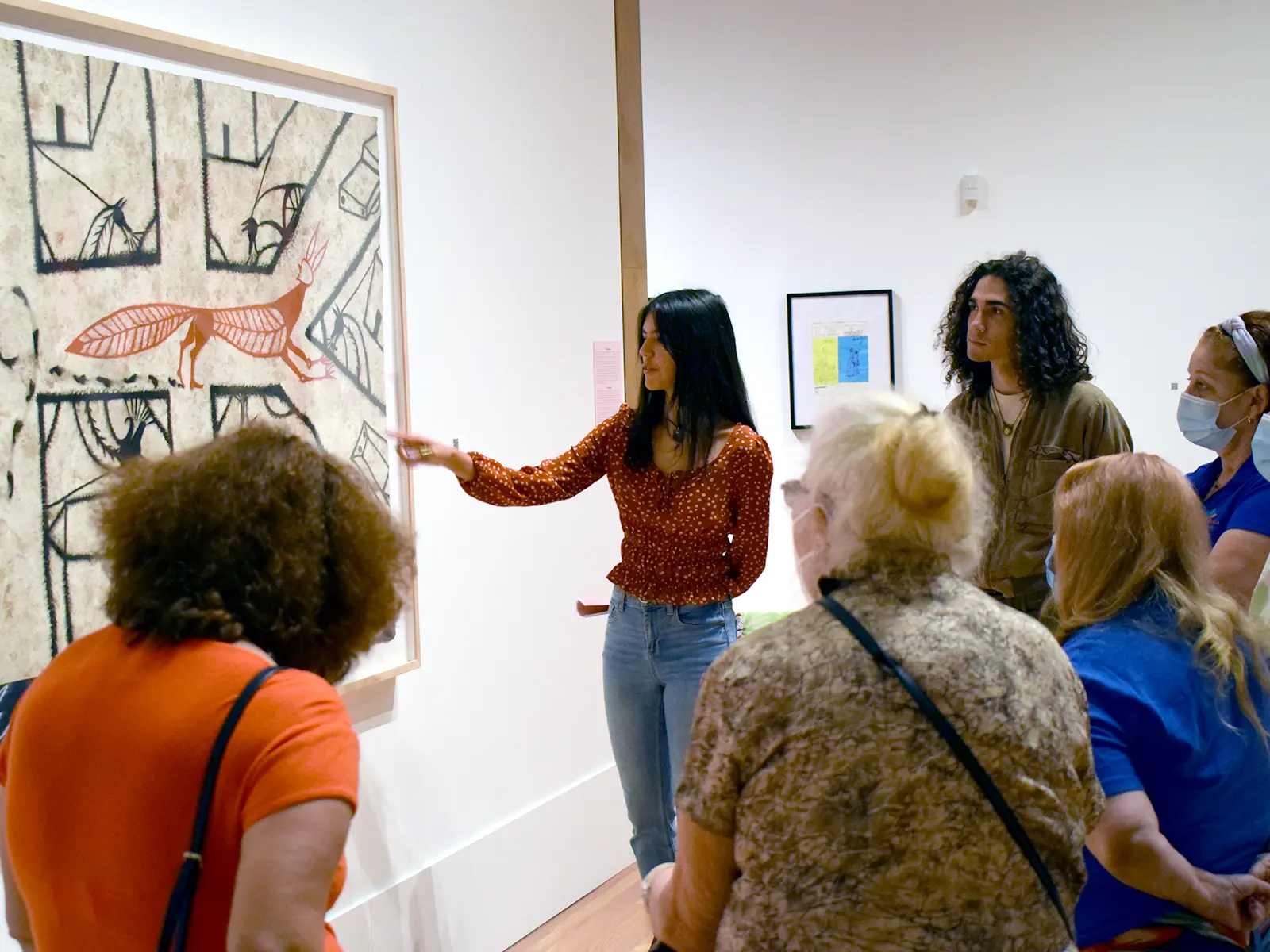 Group of individuals in an art gallery, with a guide explaining about the black and white photographs displayed on the wall.